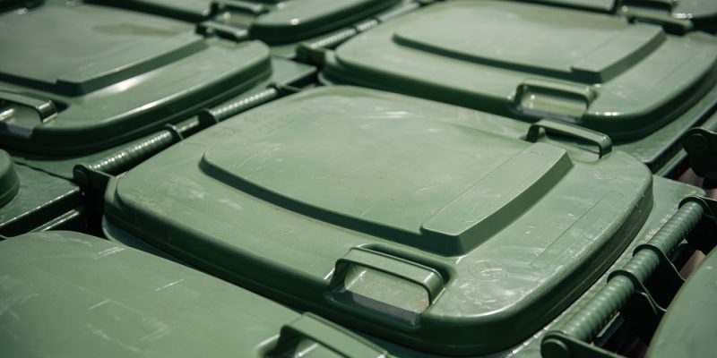 Daudzi zaļi plastmasas atkritumu konteineru vāki izvietoti rindās, redzami tuvplānā.