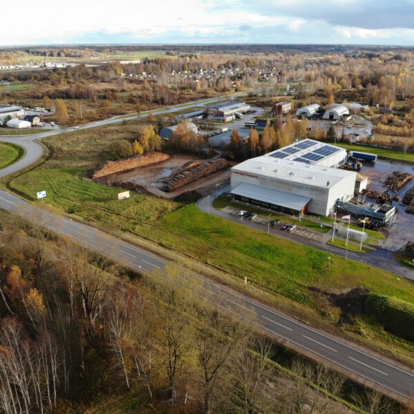 Aerofotogrāfija attēlo rūpniecisku kompleksu ar lielu ēku, uz kuras fasādes redzams uzraksts "Enerģijas pētīnieki", un saules paneļiem uz jumta. Apkārt ēkai ir milzīgas baļķu kaudzes, ceļi, transportlīdzekļi un rudens koki.